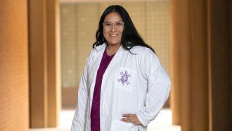 A photograph of Krystal Tsosie smiling in her white lab coat, which has an embroidered tortoise on it.