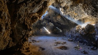 An illustration of a rover exploring a lava tube with light streaming through the top