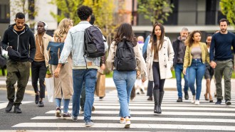 A group of people of various races and ethnicities crossing a street