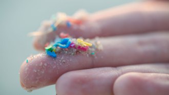 Bits of colorful microplastics lay on the tips of a white person's outstretched fingers.