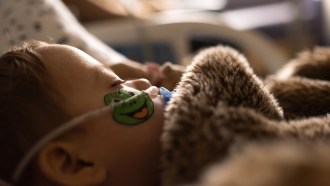 A close up photo of a toddler laying in a bed with a tube attached to his nose.