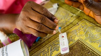 A nurse's hand drops human blood on a small, white plastic malaria rapid test.