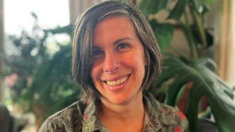 A headshot of Marjorie Weber smiling in front of large plants