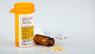 A pill bottle with a fentanyl label sits next to several pills and a vial on a table