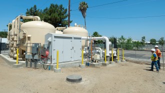 An outdoor view of an apparatus that removes chemicals from the public water supply. Two men in hardhats look on.