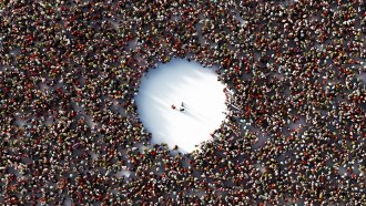 A packed crowd with a giant empty circle in the middle is shown from above. Three people stand in the empty space..