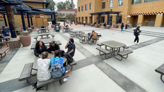 A photo of an outdoor space with tables with a few university students sitting at some of the tables.