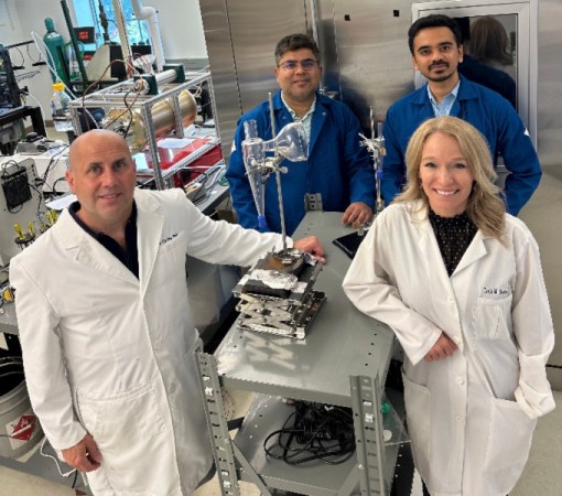 A photo of three men and one woman standing around a table with the SARS-CoV-2 detector they developed (clockwise from front left: John Cirrito, Rajan Chakabarty, Joseph Puthussery and Carla Yuede).