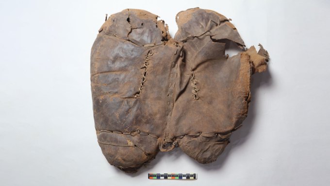 An ancient saddle against a white backdrop with a colorful bar for scale