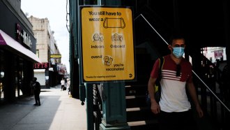 A man wearing a surgical mask passes a sign that reads "you still have to wear a mask"