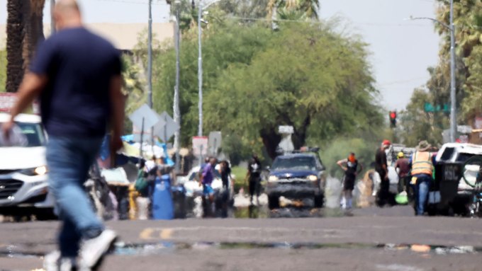 A photo of a busy street with people walking around and cars on the road. Heat haze can be seen on the road.