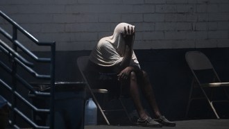 A man sitting in a dark gymnasium with a wet towel draped over his head and upper body.