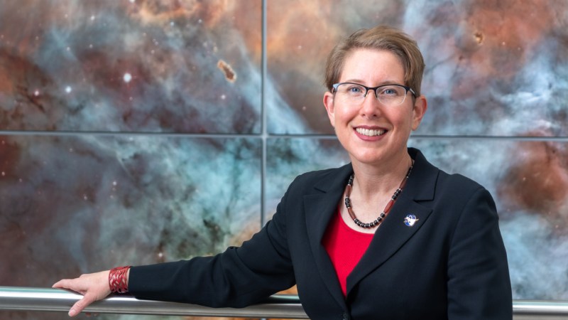 A photo of Jane Rigby standing in front of a large galaxy image.