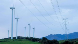 A photo of wind turbines in a grassy area with power lines nearby.