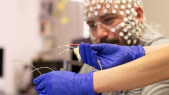 A photo of the connector cords used for external electrodes on a cap which can be seen on a man's head in the background.