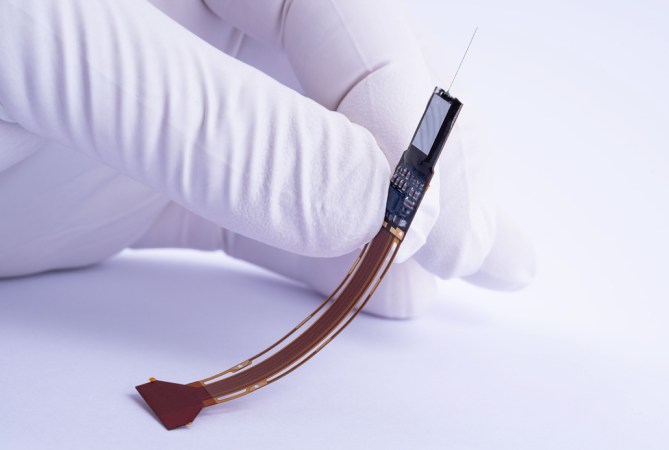 a gloved hand holds a roughly two-inch long device