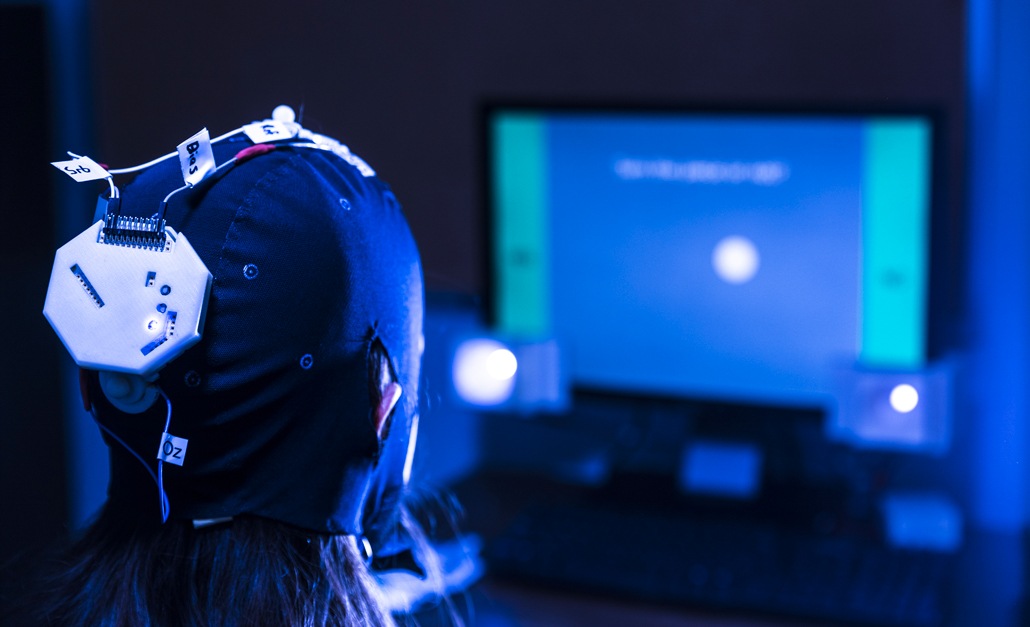 A person wearing a tight-fitting device on her head looks at a computer screen