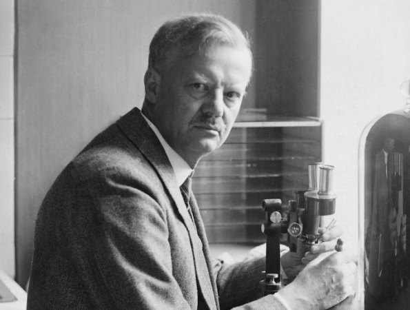 black and white photograph of a man looking at the camera and holding a microscope