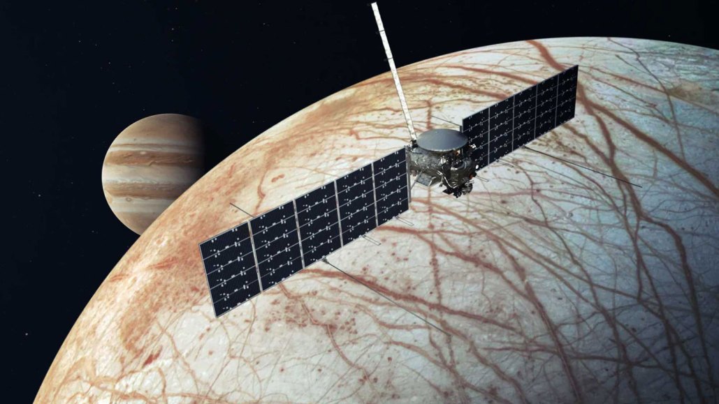 An illustration of the Europa Clipper spacecraft in front of the moon Europa, which is pale with red stripes crisscrossing the surface. Jupiter peeks out from behind Europa.